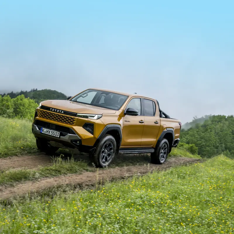 Gele Toyota Hilux pick-up op een onverhard pad door een weide
