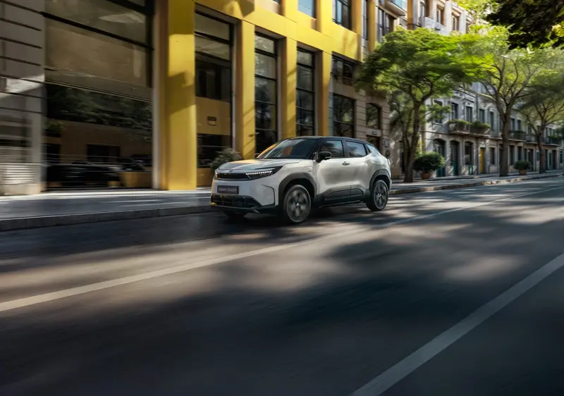 Witte Toyota Urban Cruiser rijdt door een stadsstraat met gele gebouwen