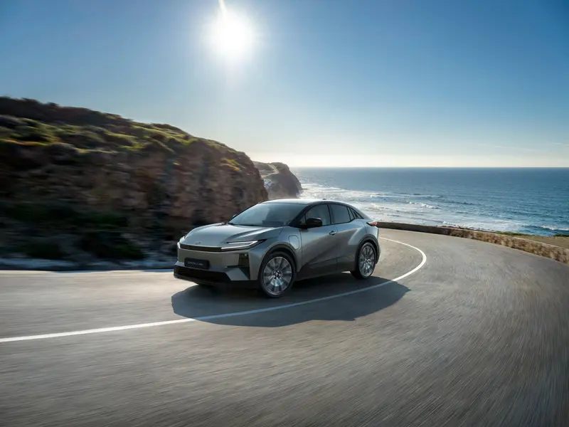 Toyota C-HR+ in het grijs rijdt over een kustweg langs de zee